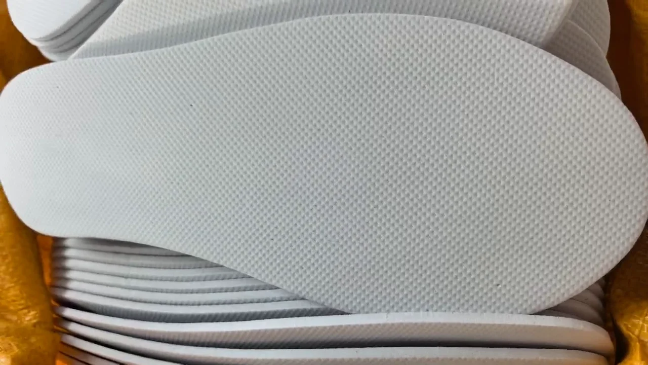 Full white die-cut EVA hotel slipper sole with a fine diamond non-slip texture, lying on a stack of soles in a woven bag