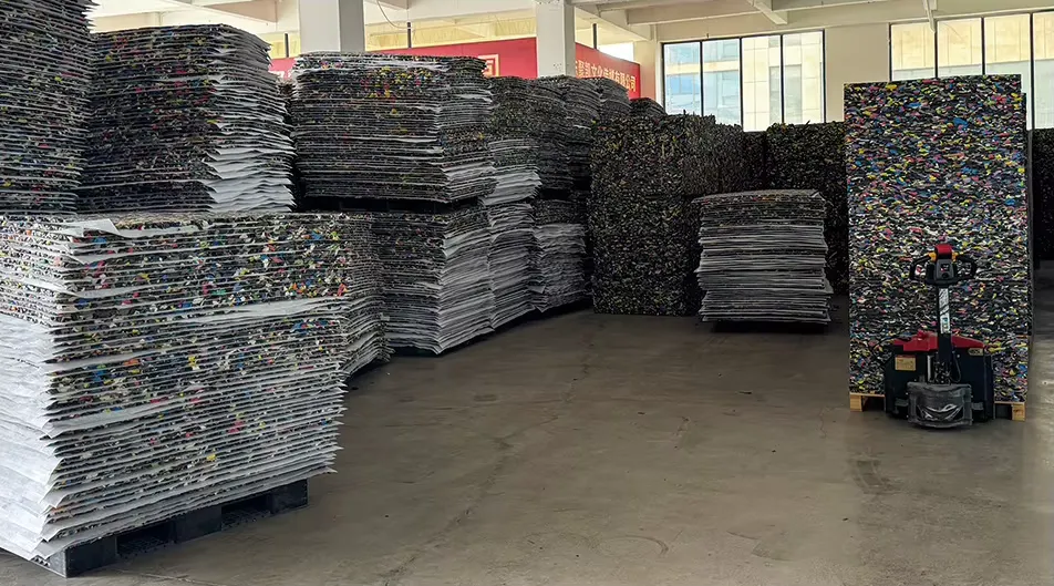 Stacks of rebonded EVA turf shock pad sheets in the SANSD warehouse, waiting to be palletized