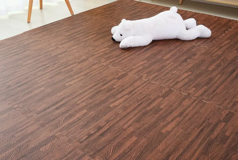 Dark walnut wood-grain EVA puzzle mats covering a living room floor, with a plush toy on top